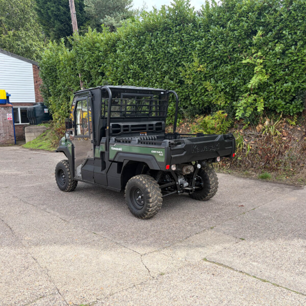 Green Kawasaki Diesel 4x4 utility vehicle in a parking area, with a yellow Russell’s sign storefront to the left and a tall green hedge behind it.
