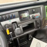 Truck dashboard with ignition key, digital display, and row of switches; green body panel visible outside.
