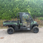 Green Kawasaki Diesel 4x4 utility vehicle parked on a road with a tall green hedge behind it.