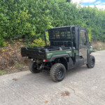 Kawasaki diesel 4x4 utility vehicle parked on a road beside a tall green hedge.