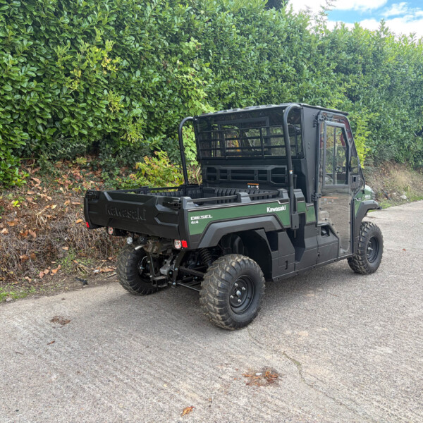 Kawasaki diesel 4x4 utility vehicle parked on a road beside a tall green hedge.