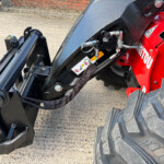 Close-up of a hydraulic attachment on a red construction machine, showing hoses, fittings, and a black metal arm.