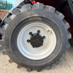 Close-up of a large tractor tire with deep, chunky treads and a silver wheel in an outdoor setting behind a fence.