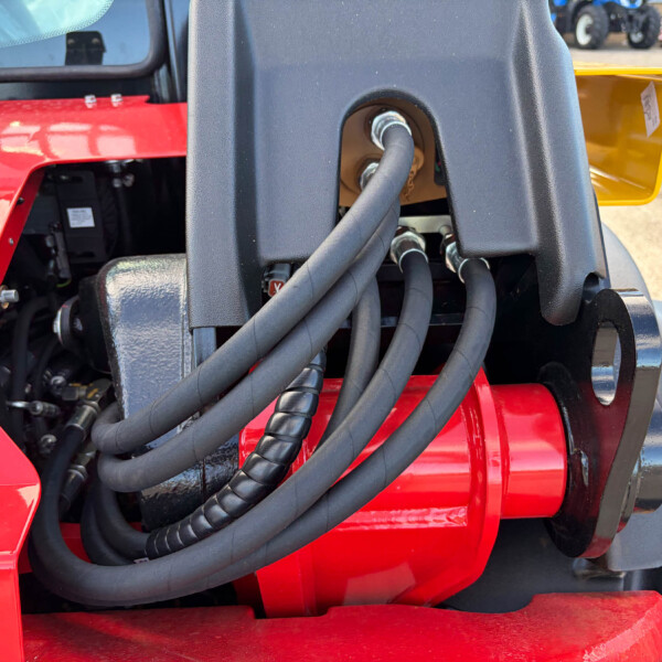 Close-up of thick hydraulic hoses bundled on red farm machinery, with a black frame nearby.