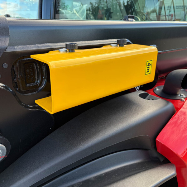 Close-up of a yellow rectangular control housing with two black knobs on top mounted to a dark machine chassis, part of heavy equipment.