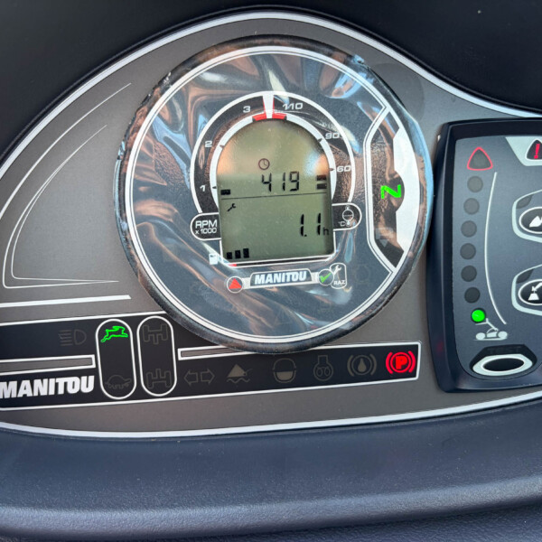 Close-up of a motorcycle instrument cluster with a circular tachometer, digital display, and green neutral indicator; MANITOU branding visible on the panel.