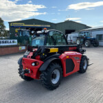 Red Manitou tractor in the foreground at an agricultural equipment yard with a Russell's Agriculture building in the background and other tractors nearby.