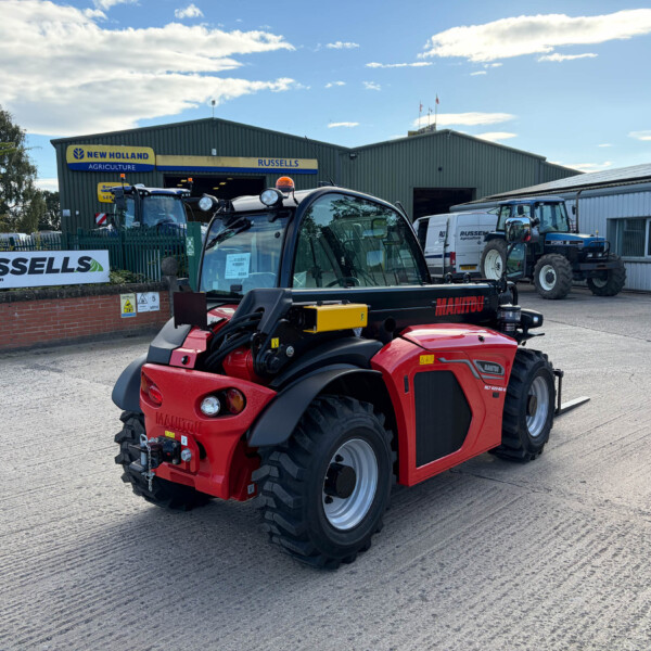 Red Manitou tractor in the foreground at an agricultural equipment yard with a Russell's Agriculture building in the background and other tractors nearby.