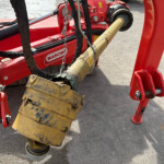 Red industrial machine with a large yellow hydraulic attachment suspended by chains, resting on an asphalt surface