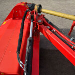Close-up of red hydraulic machinery with black hoses and a large yellow rod attached to a metal frame on a concrete surface.