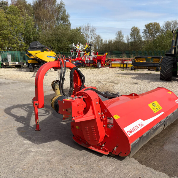 Large red farming implement (Graffa XXL) in foreground at an outdoor machinery yard, with green tractors and various red and yellow equipment in the background.