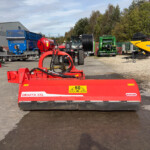 Red Graffa XXL agricultural machine in the foreground with blue, green, and yellow farming equipment parked in a yard.