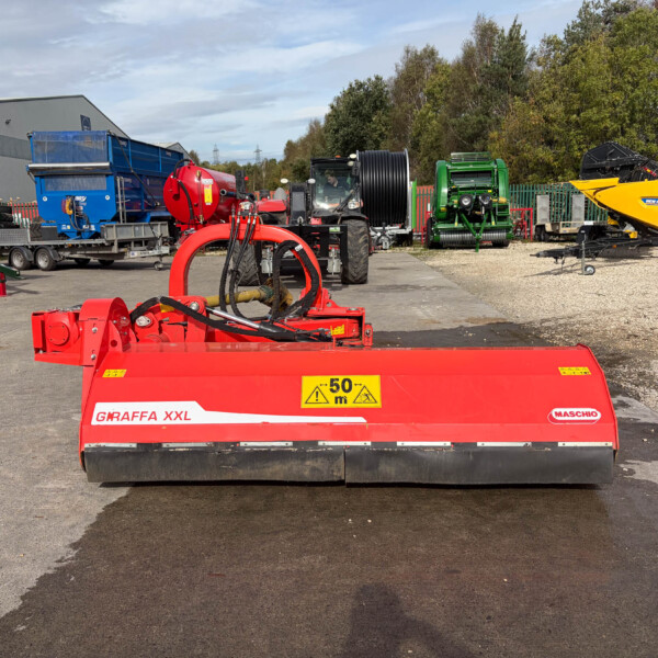Red Graffa XXL agricultural machine in the foreground with blue, green, and yellow farming equipment parked in a yard.