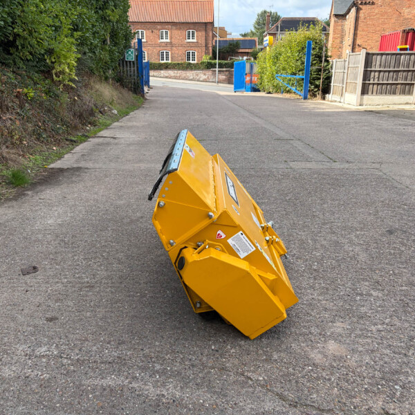Overturned yellow road safety barrier on a paved street, with blue gates and brick buildings in the background outside a construction area.
