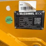 Close-up of a yellow machine with a black MCCONNEL plate, bar code sticker, and a green "PASSED INSPECTION" sticker visible on the surface.