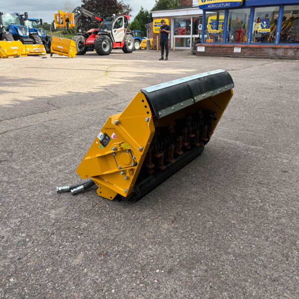 Yellow industrial roller attachment on a parking lot with tractors and a storefront in the background.