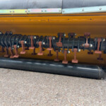 Close-up of a rust-colored rotor with mounted brackets and bolts inside a yellow agricultural machine housing.