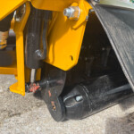 Close-up of a yellow hydraulic machine arm with bolts and a black suspension component on heavy equipment (construction machinery).