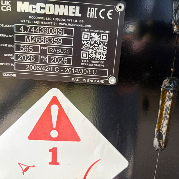 Close-up of an industrial nameplate with model and serial numbers on a dark surface, plus warning triangle decals nearby, hinting at caution around the equipment.