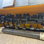 Close-up of a yellow agricultural implement with black rotating tines and metal components
