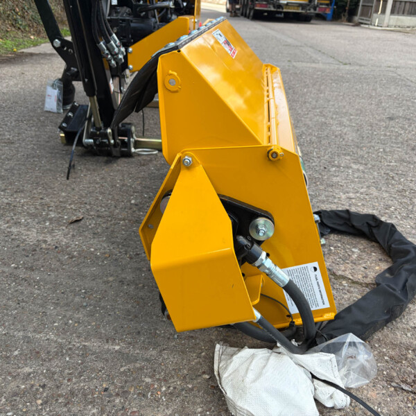 Yellow hydraulic attachment mounted on a construction machine, resting on a paved surface with hoses and metal bolts visible.