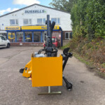 Exterior view of a Russell's shop with New Holland signage, and a large yellow industrial machine in the foreground; a white van is parked to the left.