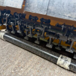 Close-up of a yellow machine housing with black rotating shafts, cams, and metal linkage components underneath.