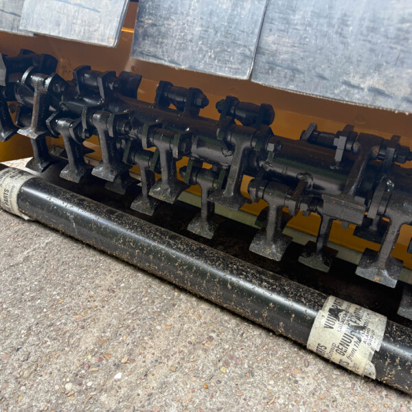 Close-up of a yellow machine housing with black rotating shafts, cams, and metal linkage components underneath.