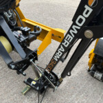 Close-up of a yellow metal frame with hydraulic hoses, fittings, and a black motor component on heavy machinery.