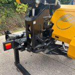 Close-up of a yellow construction machine showing a hydraulic cylinder and black frame on a concrete surface.