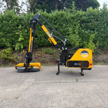 Compact yellow and black hydraulic lifting arm machine parked on a paved surface with a green hedge in the background, McConnel branding visible on the side.