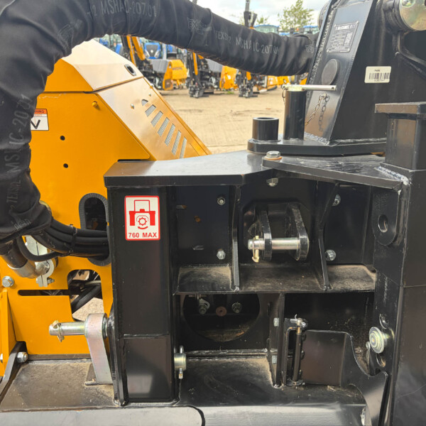 Close-up of yellow and black heavy construction equipment showing hydraulic hoses, bolts, and safety labels like 760 MAX.