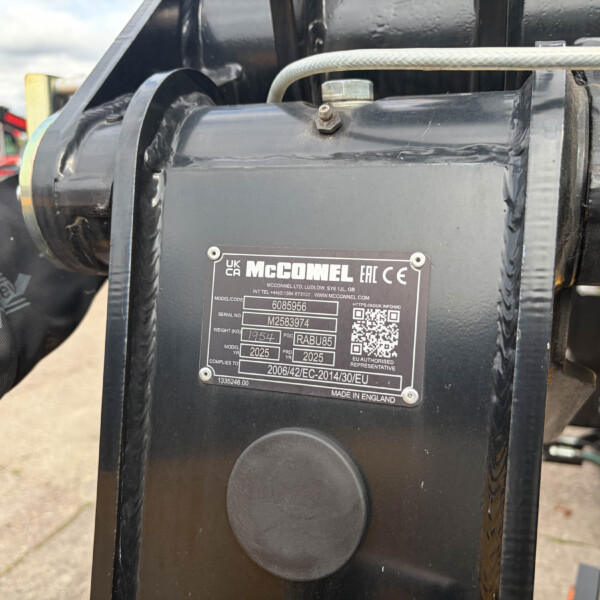 Close-up of a black hydraulic implement with a metal nameplate reading 'McCONNEL' and a bolt, showing part of the linkage.