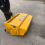 Close-up of a yellow McConnel attachment connected to a hydraulic excavator on a cracked asphalt surface.