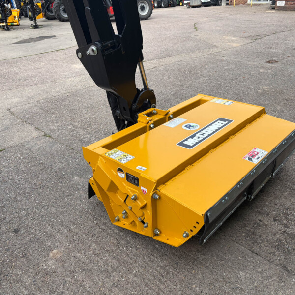 Close-up of a yellow hydraulic excavator/bucket attachment mounted on a black arm, in a lot with other equipment in the background