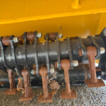 Close-up of rusted metal rollers and bolts on a yellow farm implement, showing corrosion and mounting brackets on a rotating frame.