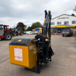 Close-up of a yellow industrial machine with warning stickers in a machinery lot, with red and gray tractors and a Russell's store in the background.