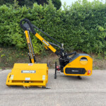 Yellow McConnel landscaping machine with a mower attachment, parked on a paved surface with a green hedge in the background,