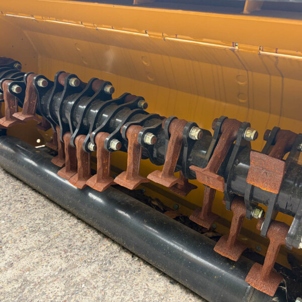 Close-up of a rusted mechanical linkage with bolt joints inside a yellow agricultural machine.