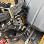 Close-up of a heavy machinery hydraulic system with hoses, metal brackets, and warning labels on a black frame.