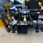 Close-up of a yellow industrial machine showing hydraulic mounting with hoses, bolts, and labels in view of a heavy-duty assembly.