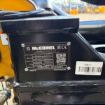 Close-up of a black metal control housing with a McCONNEL identification plate, barcode and QR area, mounted on yellow machinery.