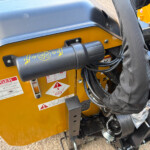 Close-up of a yellow construction machine panel with a black control lever, safety stickers, and bundled cables nearby.