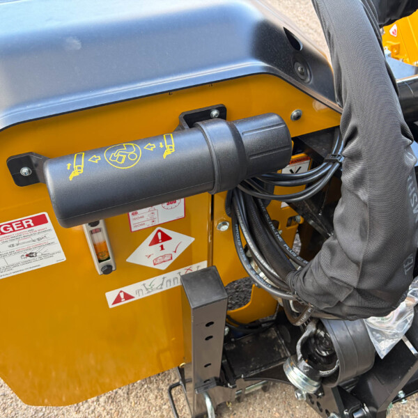 Close-up of a yellow construction machine panel with a black control lever, safety stickers, and bundled cables nearby.