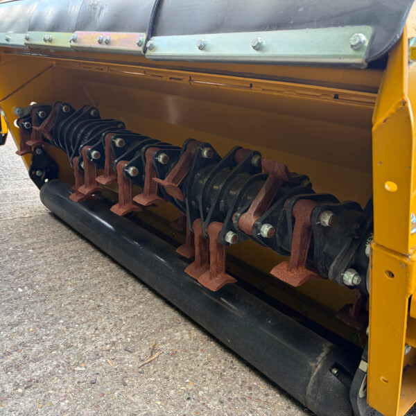 Close-up of a yellow construction machine showing a chain-driven roller assembly with rust-colored links and bolts along the baseplate.