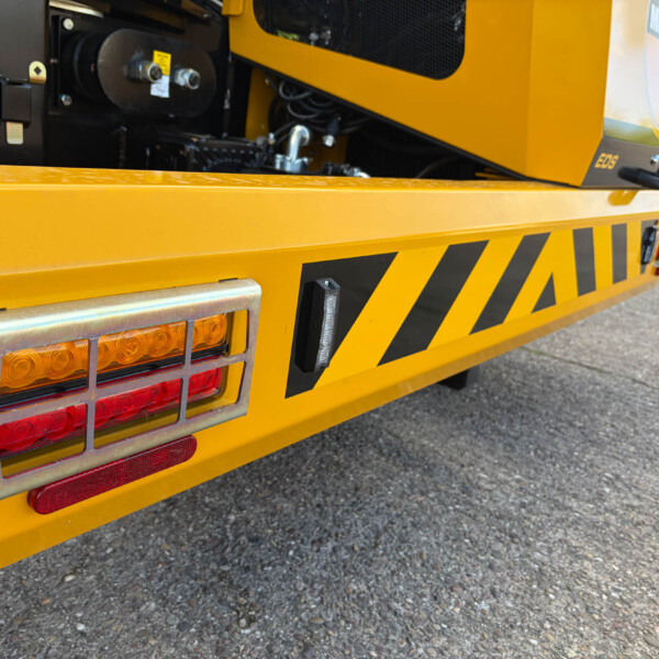 Back of a bright yellow utility truck with black hazard stripes and red/amber tail lights on a paved street.