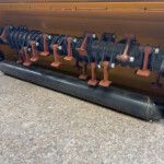 Close-up of a large rotating auger shaft with rusted mounts inside a yellow machine housing.