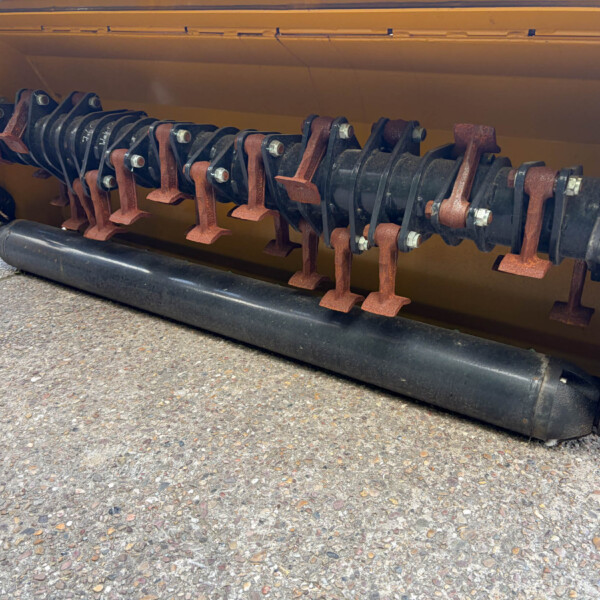 Close-up of a large rotating auger shaft with rusted mounts inside a yellow machine housing.