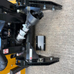 Close-up of a black metal forklift attachment with bolts, hydraulic components, and a yellow base.