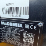 Close-up of a black metal plate with a white barcode label, a QR code, and the McConnell brand name visible on a machine panel.